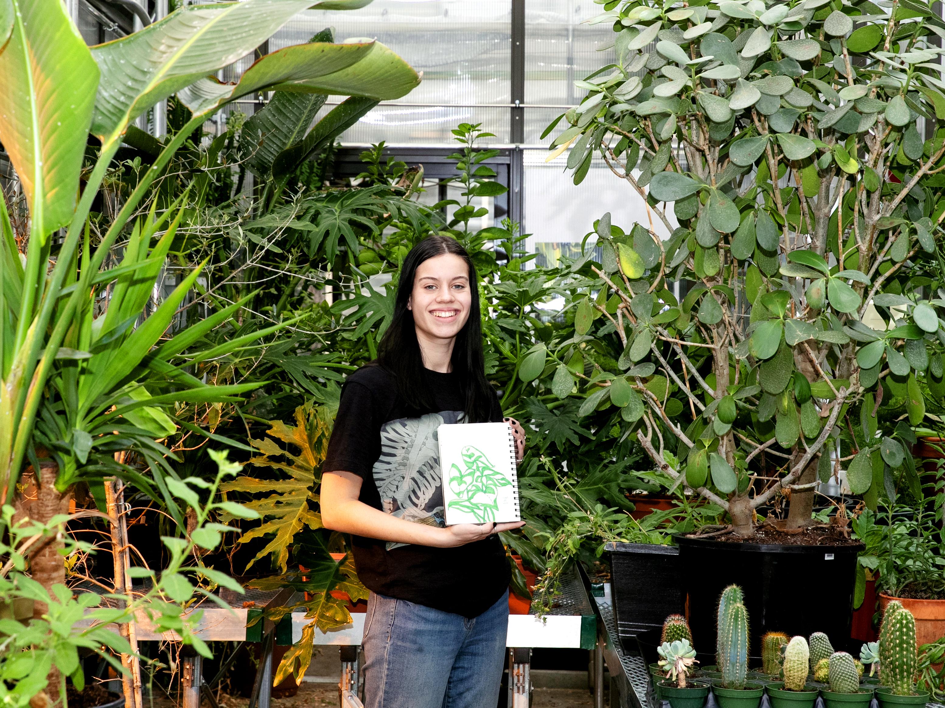 Biology and studio art double major Allison Conwell ’25, who plans to pursue a career in scientific illustration, shows one of her illustrations during a visit to the Billie Tisch Center for Integrated Sciences greenhouse.